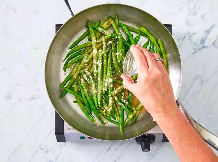 Green beans cooking in a pan as the seasonings are mixed in.