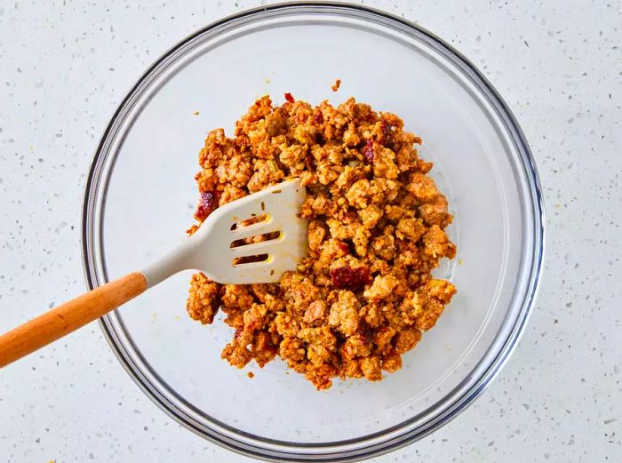 A glass bowl filled with cooked ground sausage