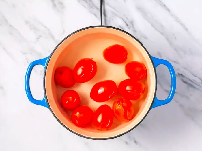 A large pot of simmering water with plum tomatoes showing cracks in their skins