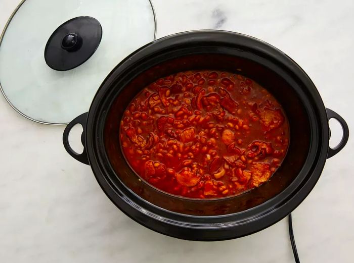 A top-down view of homemade slow-cooker baked beans, cooking away in the slow cooker.