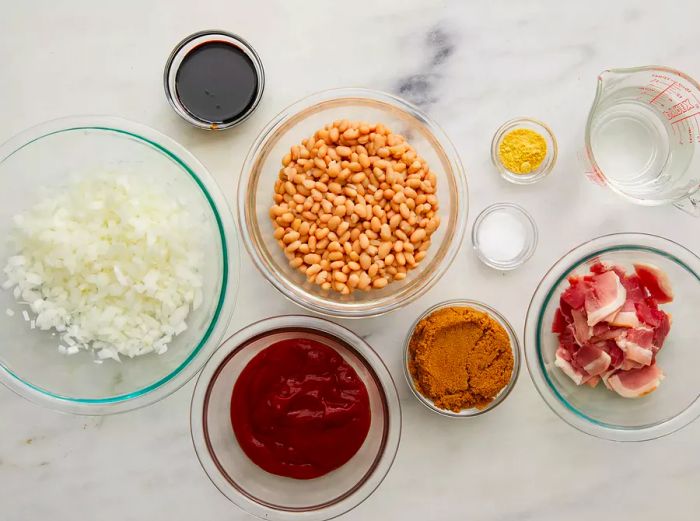 A top-down view of all the ingredients for slow-cooker beans, neatly arranged in small glass prep bowls.