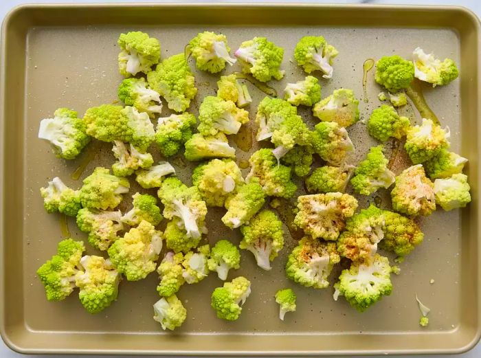 A top-down view of Romanesco on a baking sheet, topped with olive oil, black pepper, garlic powder, paprika, and salt.