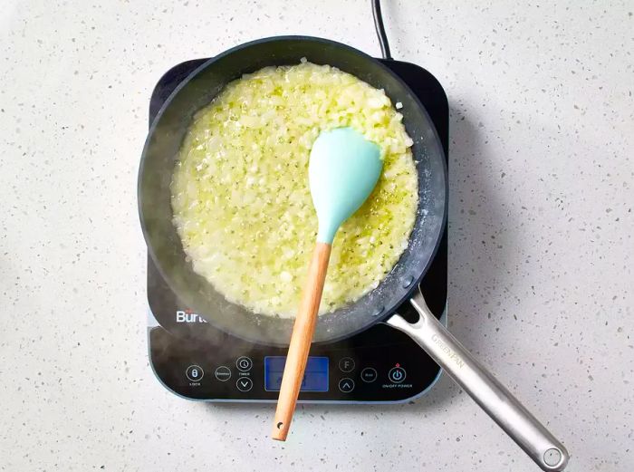 A skillet with chopped onions being stirred with a silicone spatula