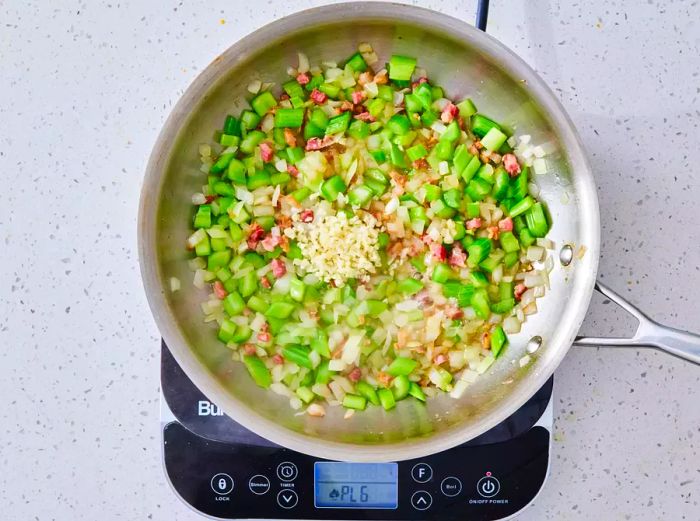 A large skillet filled with pancetta, garlic, onion, and celery