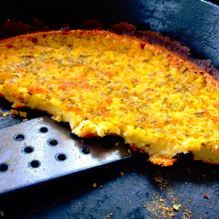 Close-up of Farinata in a cast iron skillet, with a spatula ready to serve.