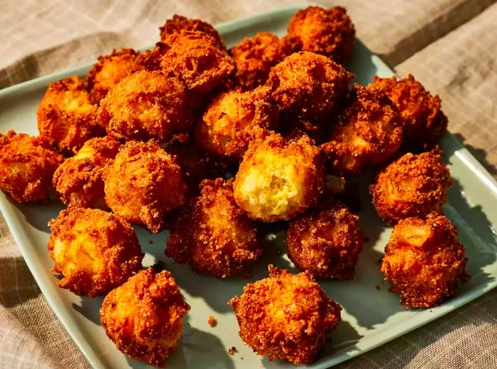 A plate of crispy, golden-brown hush puppies, with one split open to reveal the tender inside.