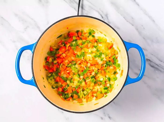 A large pot containing chopped carrots, onion, bell pepper, and garlic