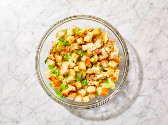 The cooked onion-celery mixture is added to the bread cubes; mix until evenly distributed.