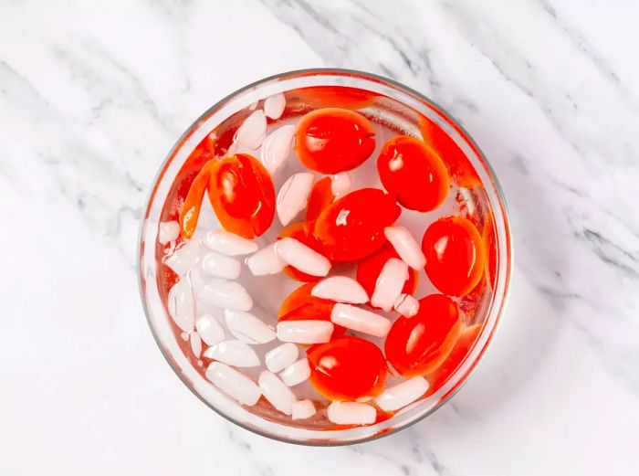 A large bowl of ice water filled with plum tomatoes showing cracked skin