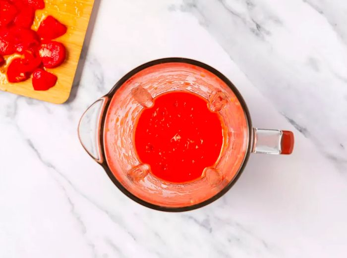 A blender filled with pureed tomatoes, placed next to a cutting board with chopped tomatoes