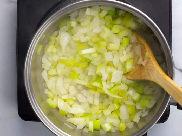 A high-angle view of onions and celery cooking in a pan.