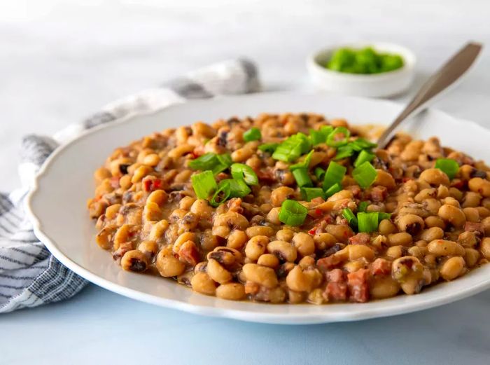 A close-up shot from a low angle of a large bowl of spicy black-eyed peas garnished with sliced green onions.