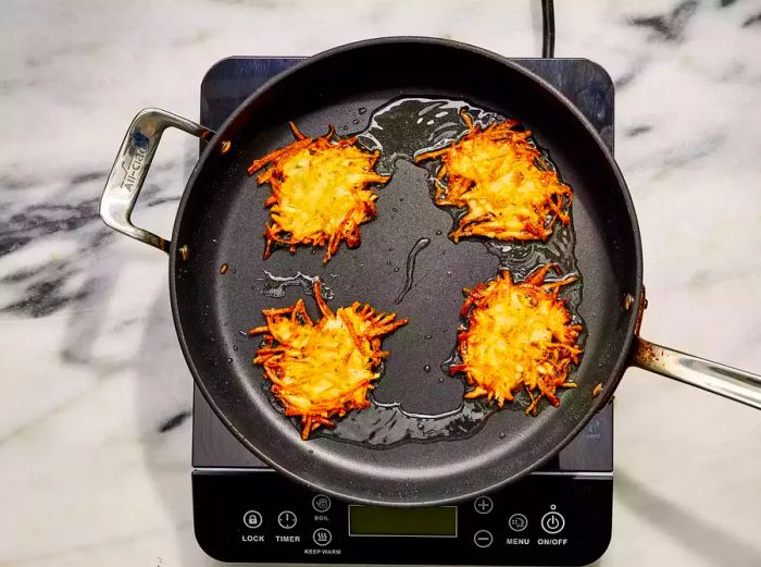 An oiled frying pan with four perfectly crispy German potato pancakes