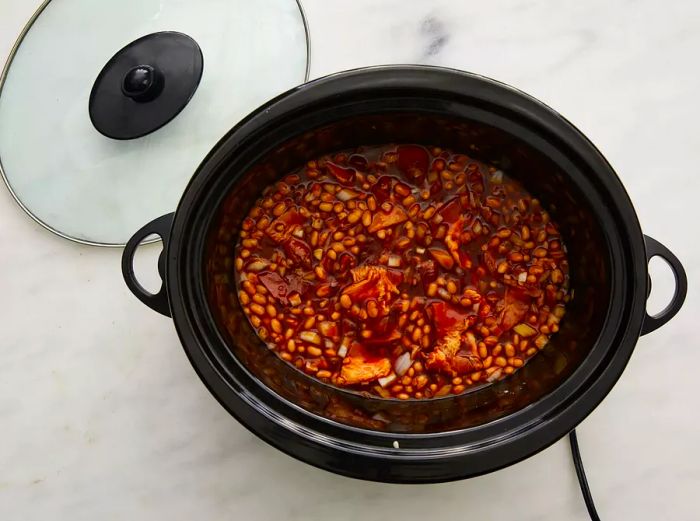 Bacon, onion, ketchup, water, brown sugar, molasses, mustard, and salt stirred into beans in the slow cooker until fully mixed.