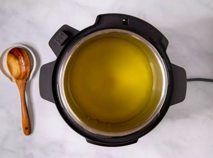 Aerial shot of a slow cooker filled with water and a dissolved bouillon cube, with a spoon placed beside it.