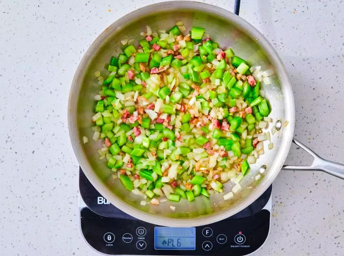 A large skillet with pancetta, celery, and onions cooking together