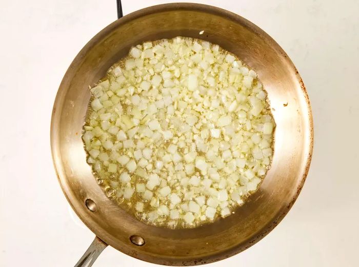 A top-down view of olive oil, onion, garlic, and lemon juice sizzling in a skillet