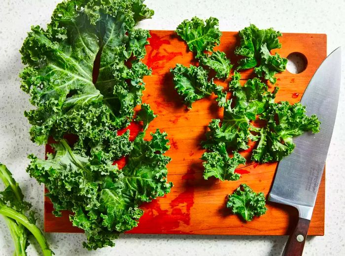 A high-angle photo of kale being chopped on a cutting board.