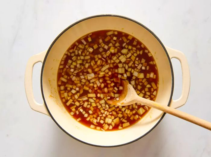 Chopped onions added to a pot with the sauce for baked beans.