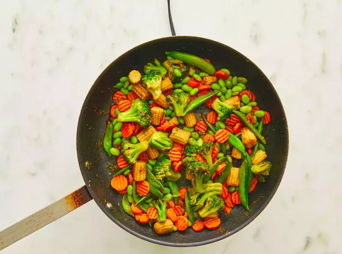 A bird's-eye view of a frozen vegetable stir-fry cooking in a large skillet.