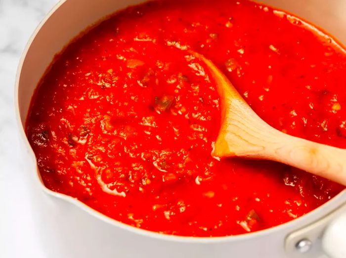 A pot of homemade tomato sauce being stirred with a wooden spoon