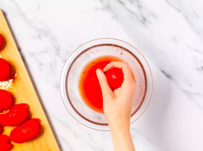 A hand gently squeezing a plum tomato over a bowl to extract the juice