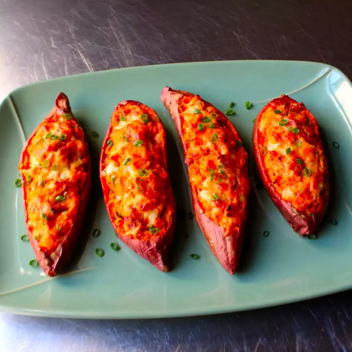 A close-up image of Loaded Twice-Baked Sweet Potatoes topped with green onions, arranged on a platter.