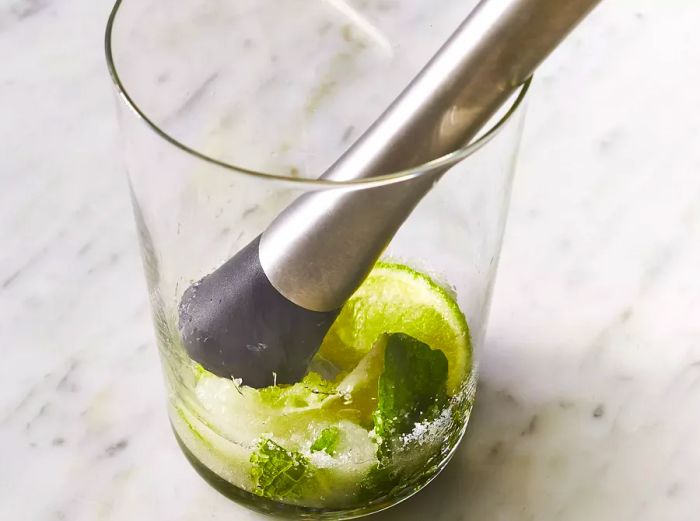 additional lime wedges and sugar being muddled in a clear glass