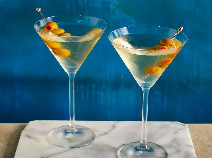 A low-angle view showcasing two vodka martinis served in classic martini glasses, each adorned with three olives.