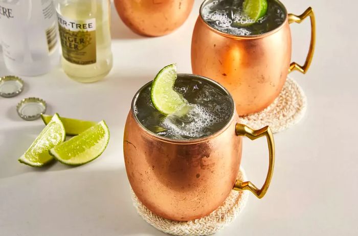 A close-up of two Moscow Mule cocktails served in classic copper mugs, each beautifully garnished with a slice of fresh lime.