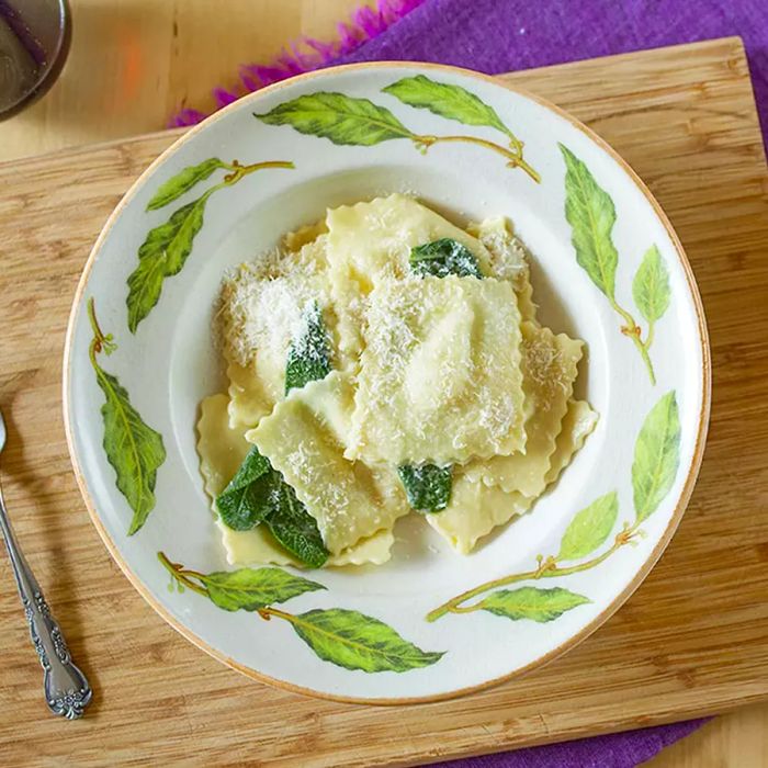 A close-up of Pear and Gorgonzola Ravioli garnished with thyme, served in a green and white bowl on a wooden cutting board.