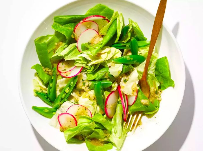 Butter lettuce with snap peas and radishes in a white bowl.