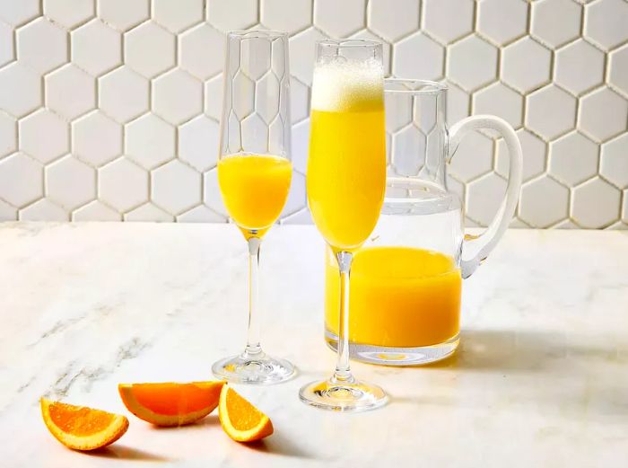 Two glasses of mimosa, served with fresh orange juice and garnished with orange slices.