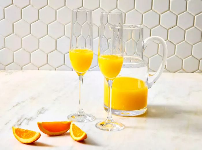 Two glasses of mimosas garnished with orange juice and slices of orange.