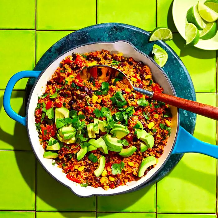 Black beans, tomatoes, and quinoa garnished with avocado and fresh herbs, all served in a turquoise skillet