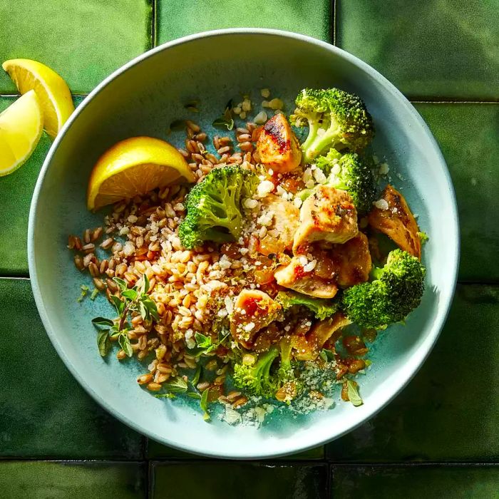 A close-up view of a lemon-parmesan chicken and farro bowl, complete with a fresh lemon wedge