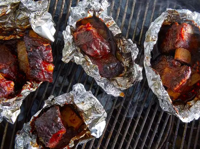 An overhead shot of cooked ribs resting in tin foil on the grill.