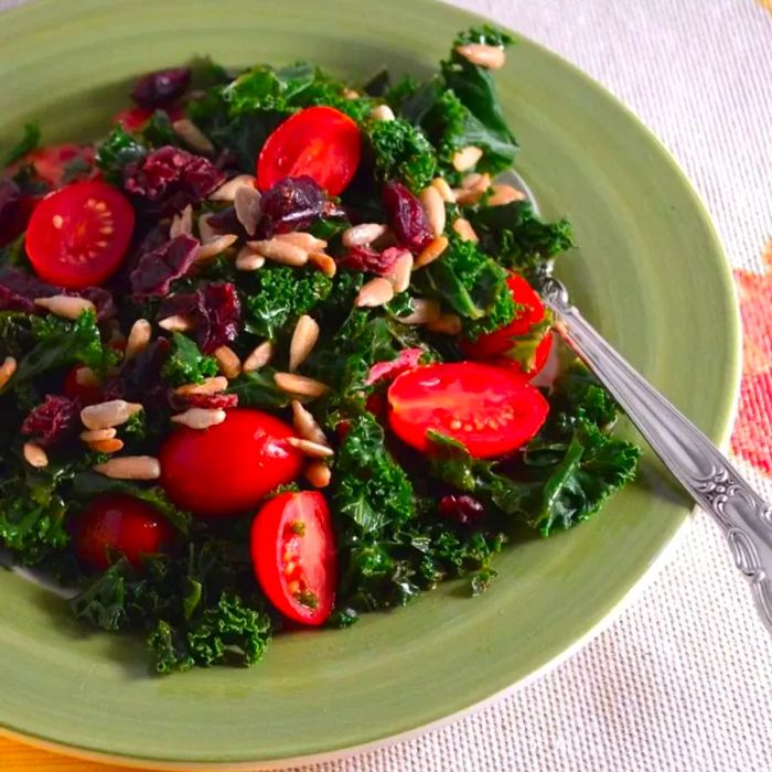 A vibrant kale salad featuring chopped kale, fresh grape tomatoes, and crunchy sunflower seeds, beautifully presented on a pale green plate.