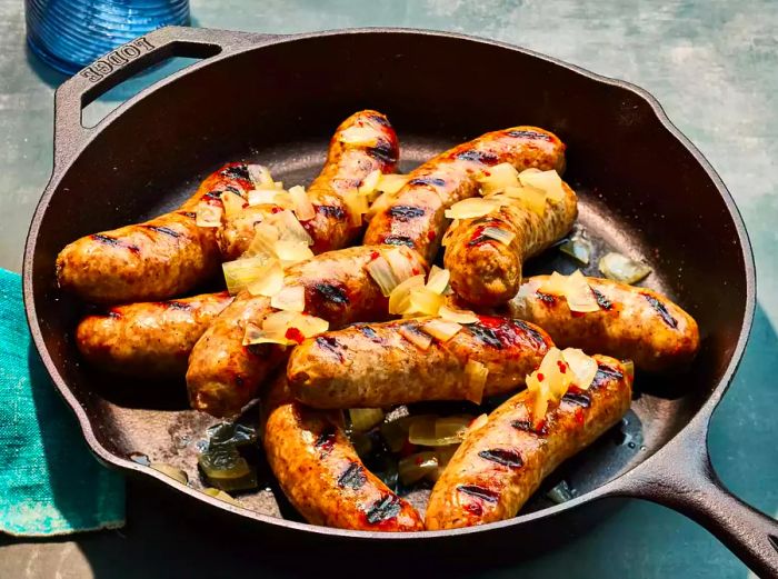 A close-up shot of Beer Brats with onions sizzling in a cast-iron skillet.