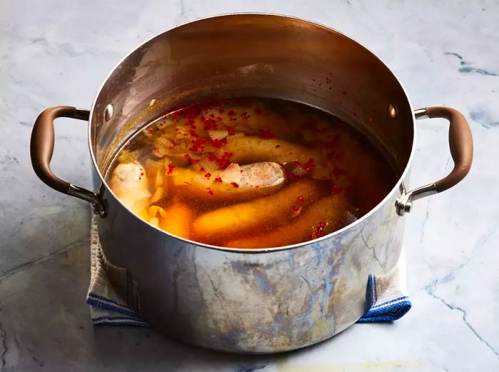 Brats floating in a beer and onion mixture inside a pot.