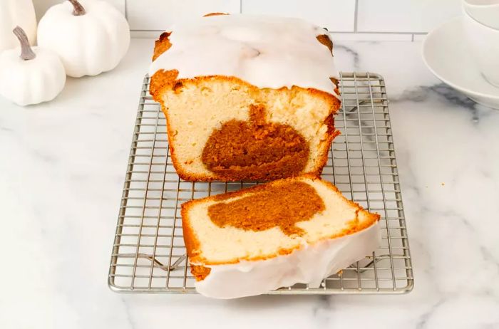 A loaf of pumpkin spice surprise cake drizzled with a confectioner's sugar glaze, sliced to reveal a hidden pumpkin-shaped pumpkin spice cake inside.