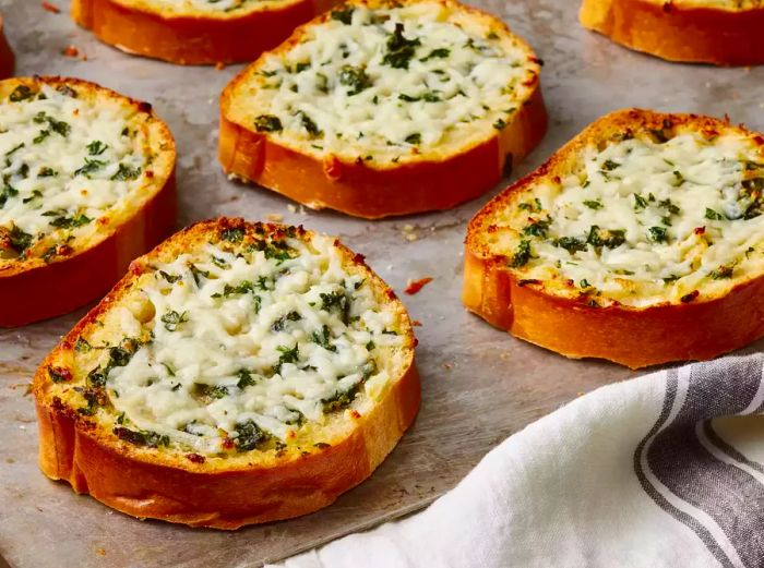 A high-angle view of a tray of garlic bread topped with melted cheese and fresh herbs.