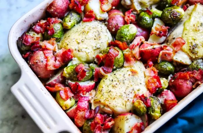 A top-down view of chicken thighs, Brussels sprouts with bacon, and roasted potatoes