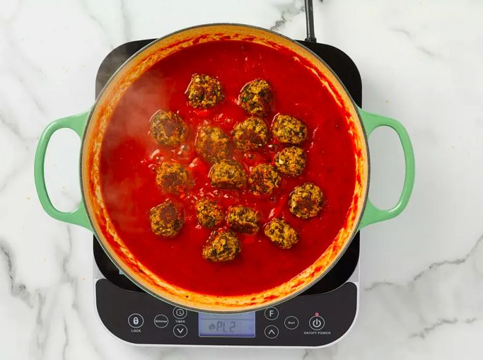 An overhead shot of meatless meatballs simmering in a rich red tomato sauce.