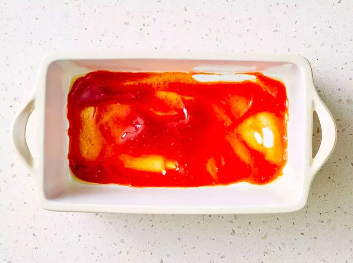 A loaf pan with a layer of sweet ketchup-brown sugar sauce at the bottom, ready for the meatloaf.