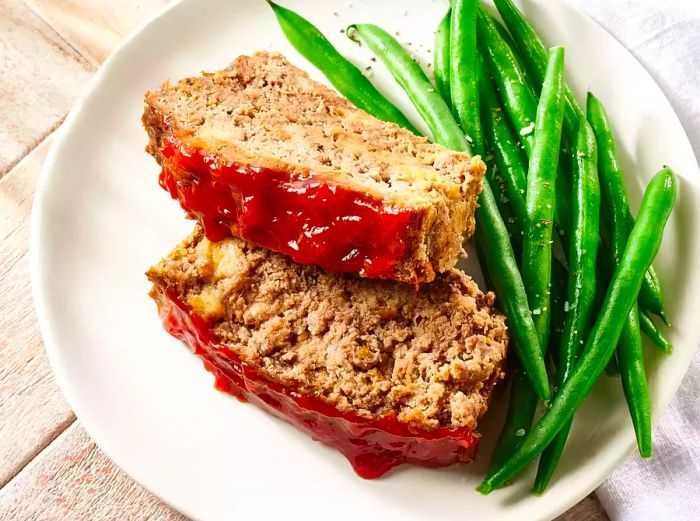 Slices of glazed meatloaf served on a plate alongside green beans