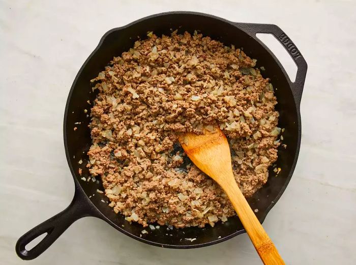 Raw onions and ground beef being sautéed together in a skillet