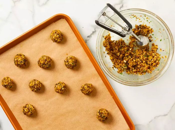 An overhead view of meatless meatballs being placed onto a parchment-lined baking sheet.