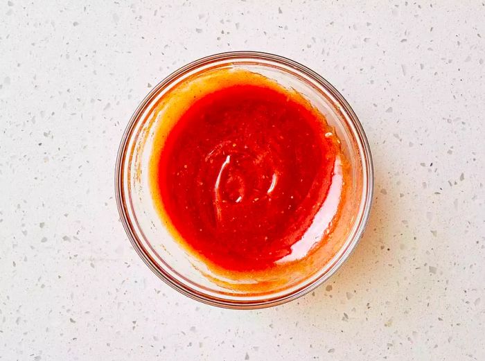 A glass bowl filled with a tangy ketchup-brown sugar sauce, seasoned to perfection.