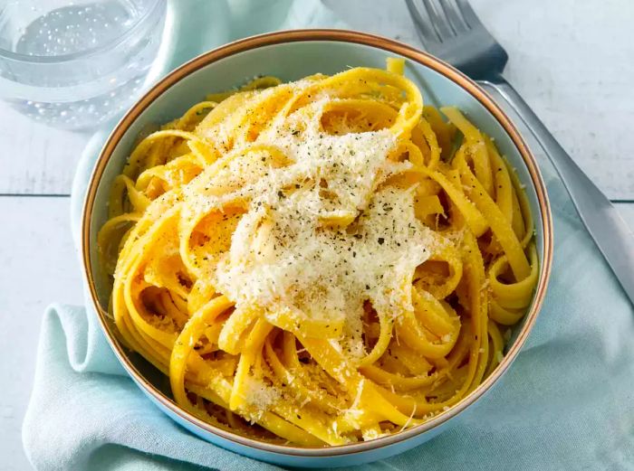 An overhead shot of buttered noodles in a bowl, topped with freshly grated cheese.